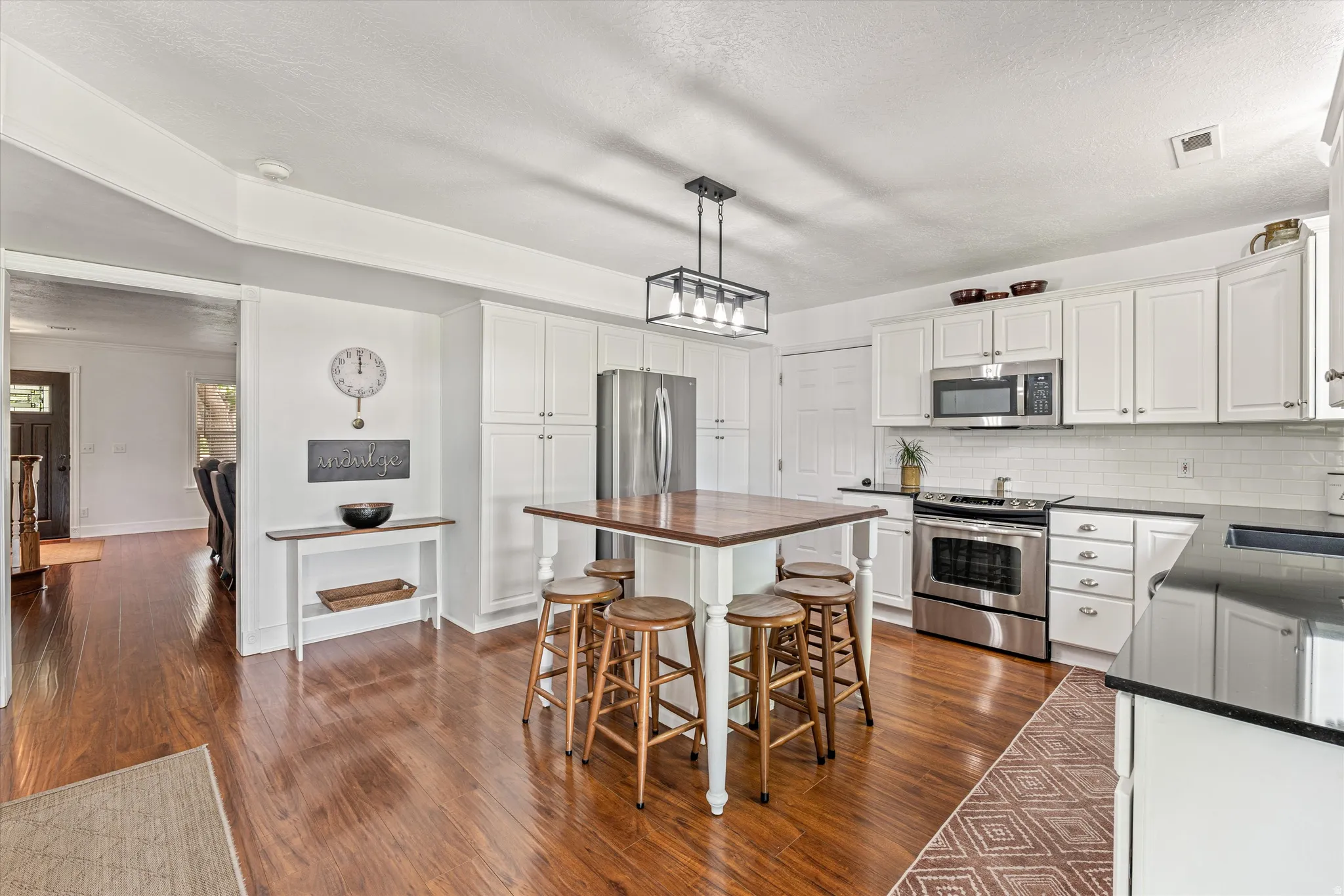 Kitchen featuring stainless steel appliances, white cabinetry, dark wood-style floors, pendant lighting, and a textured ceiling
