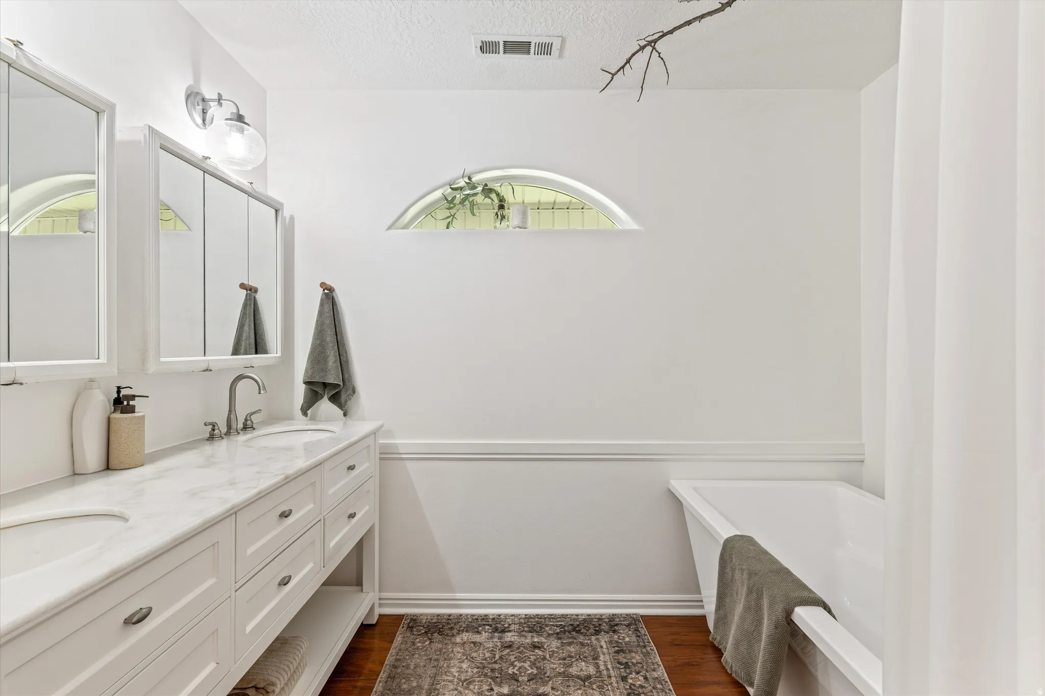 Full bathroom with a freestanding tub, double vanity, dark wood-type flooring, and a textured ceiling