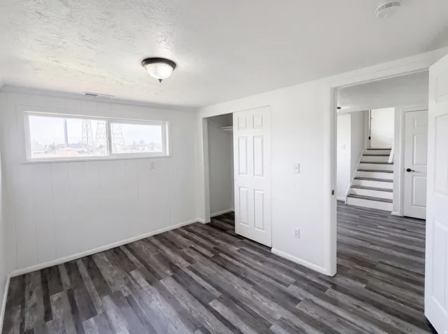 Unfurnished bedroom featuring a textured ceiling, a closet, and dark wood-style floors