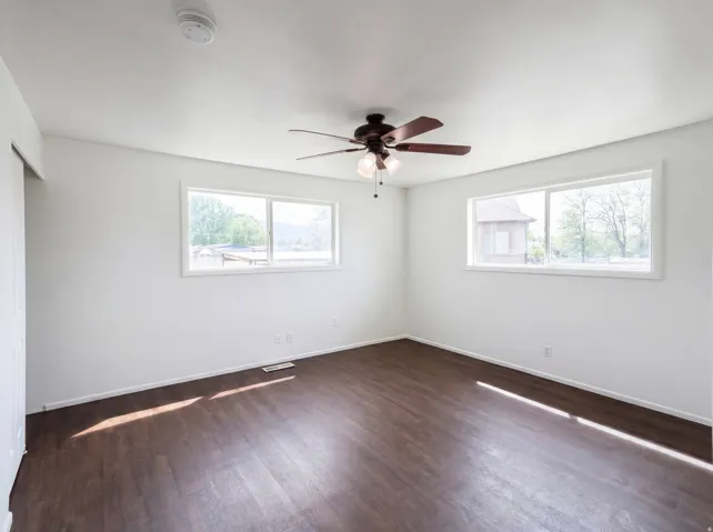 Spare room featuring dark wood-type flooring, a ceiling fan, healthy amount of natural light, and a smoke detector
