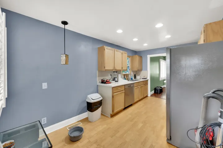Kitchen with stainless steel appliances, light wood finish cabinetry, light countertops, light wood-style flooring, and decorative light fixtures