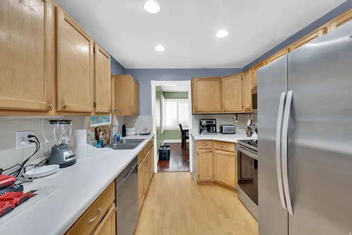 Kitchen with stainless steel appliances, light countertops, light wood finished floors, light wood finish cabinetry, and backsplash