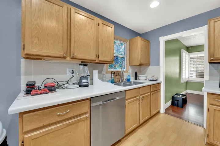 Kitchen featuring stainless steel dishwasher, light countertops, light wood-type flooring, backsplash, and light wood finish cabinetry