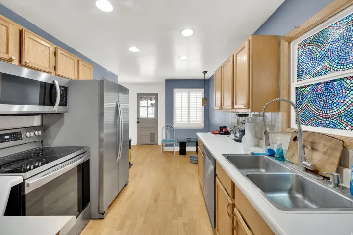 Kitchen with stainless steel appliances, decorative backsplash, hanging light fixtures, light countertops, and light wood finished floors