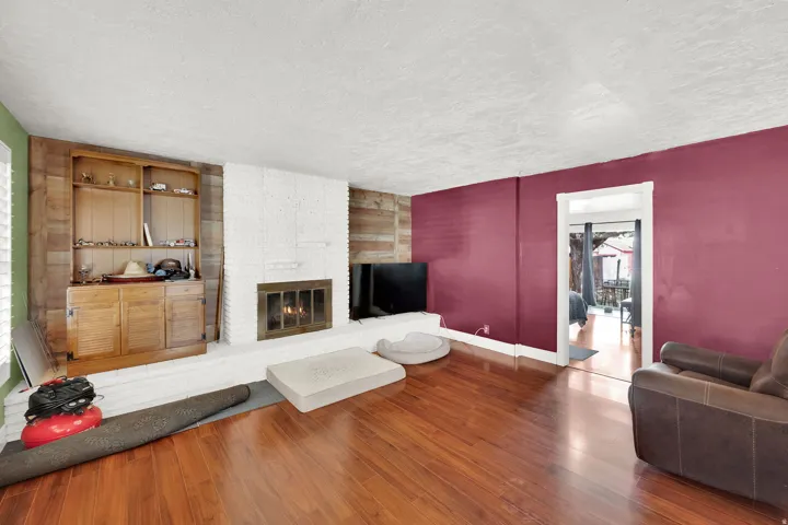 Living area featuring wood-type flooring, a textured ceiling, and a brick fireplace