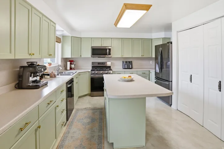 Kitchen with green cabinets, stainless steel appliances, light countertops, and a kitchen island