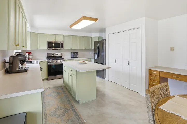 Kitchen with green cabinets, finished concrete flooring, stainless steel appliances, a center island, and light countertops