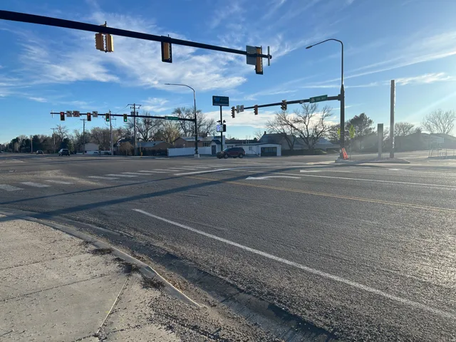 View of asphalt road with traffic lights, curbs, sidewalks, and street lighting