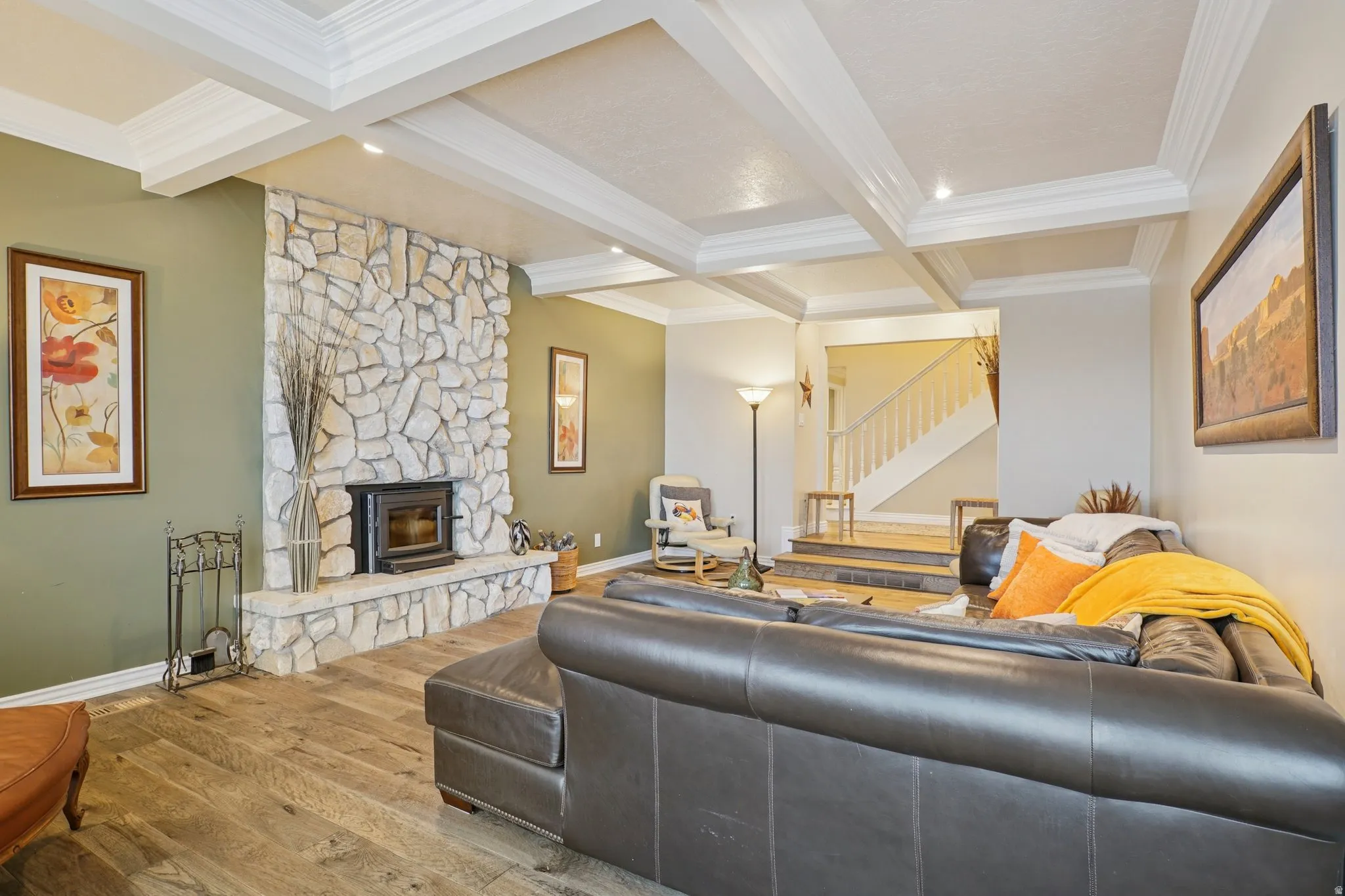 Living room featuring a stone fireplace, wood-type flooring, crown molding, and coffered ceiling