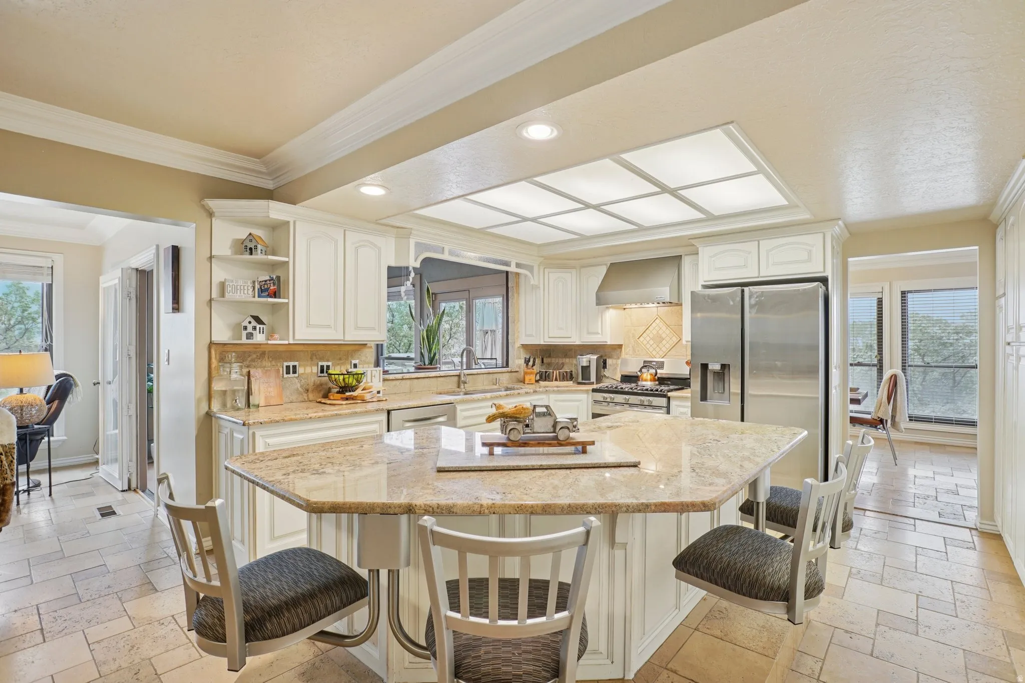 Kitchen featuring stone tile floors, plenty of natural light, ornamental molding, recessed lighting, and white cabinets