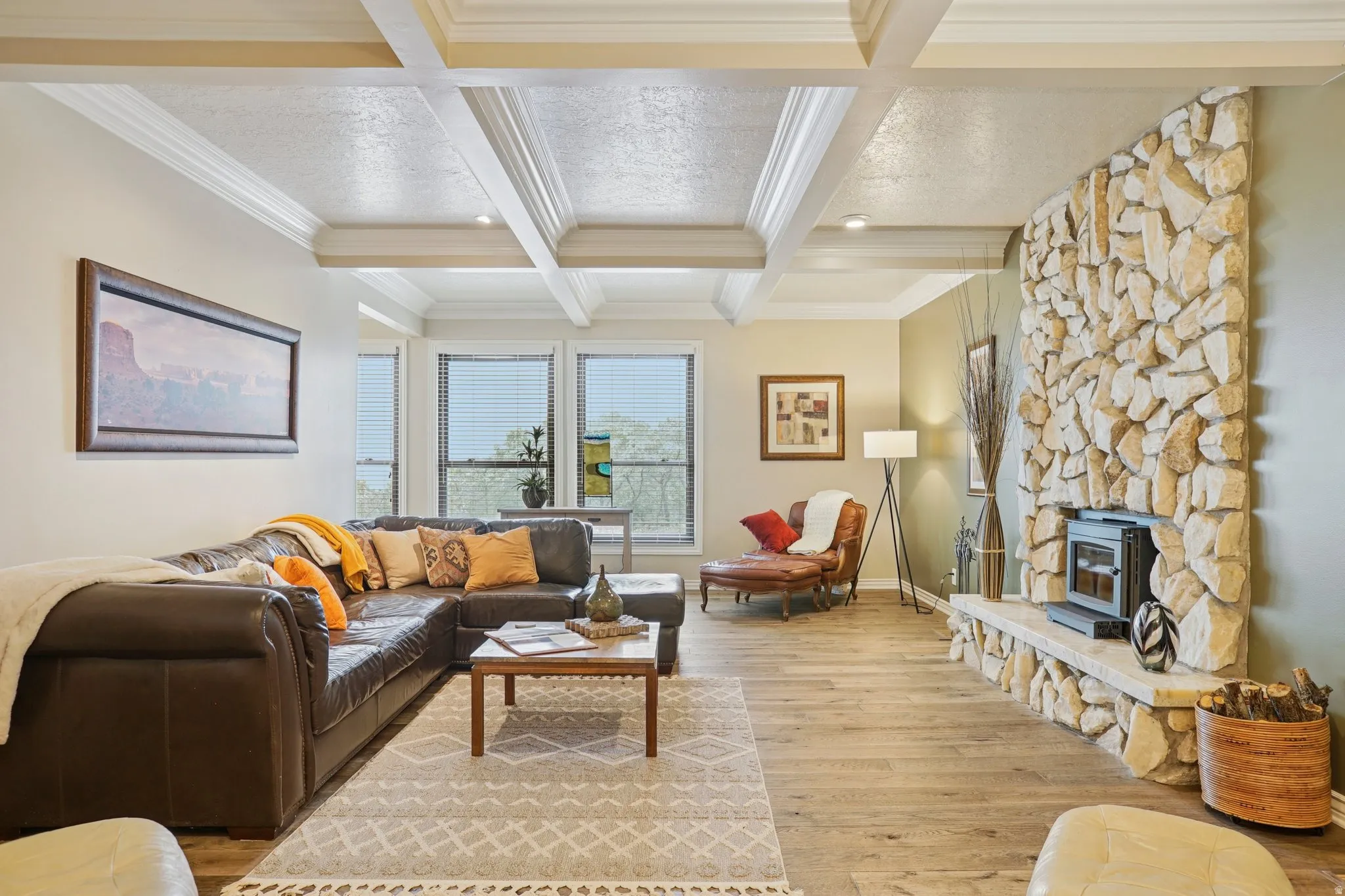 Living room featuring light wood-style floors, a wood stove, crown molding, and coffered ceiling