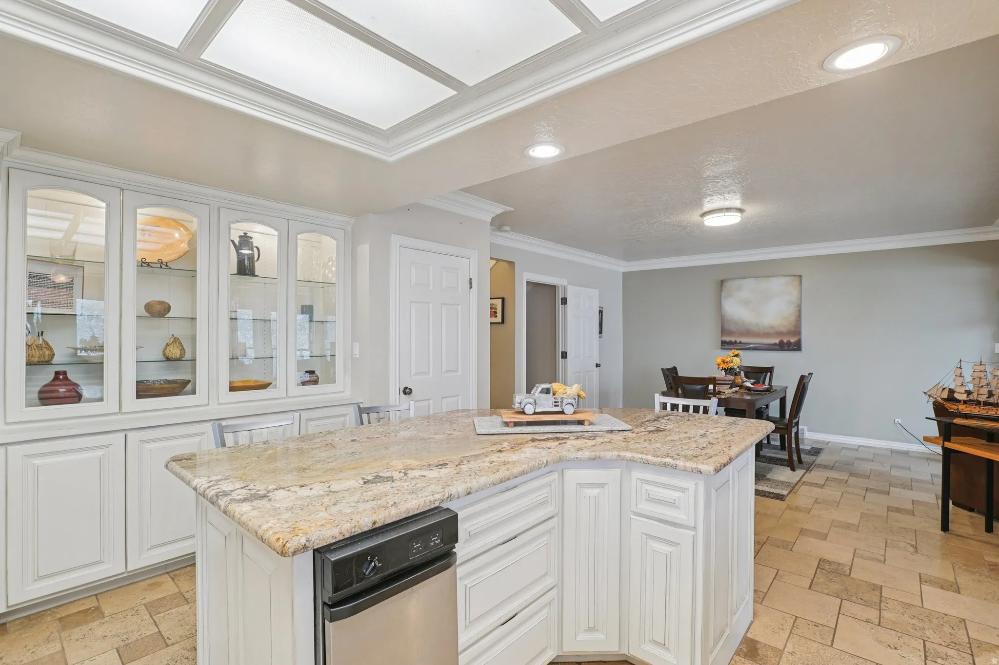 Kitchen with white cabinets, stone tile floors, glass insert cabinets, a kitchen island, and crown molding