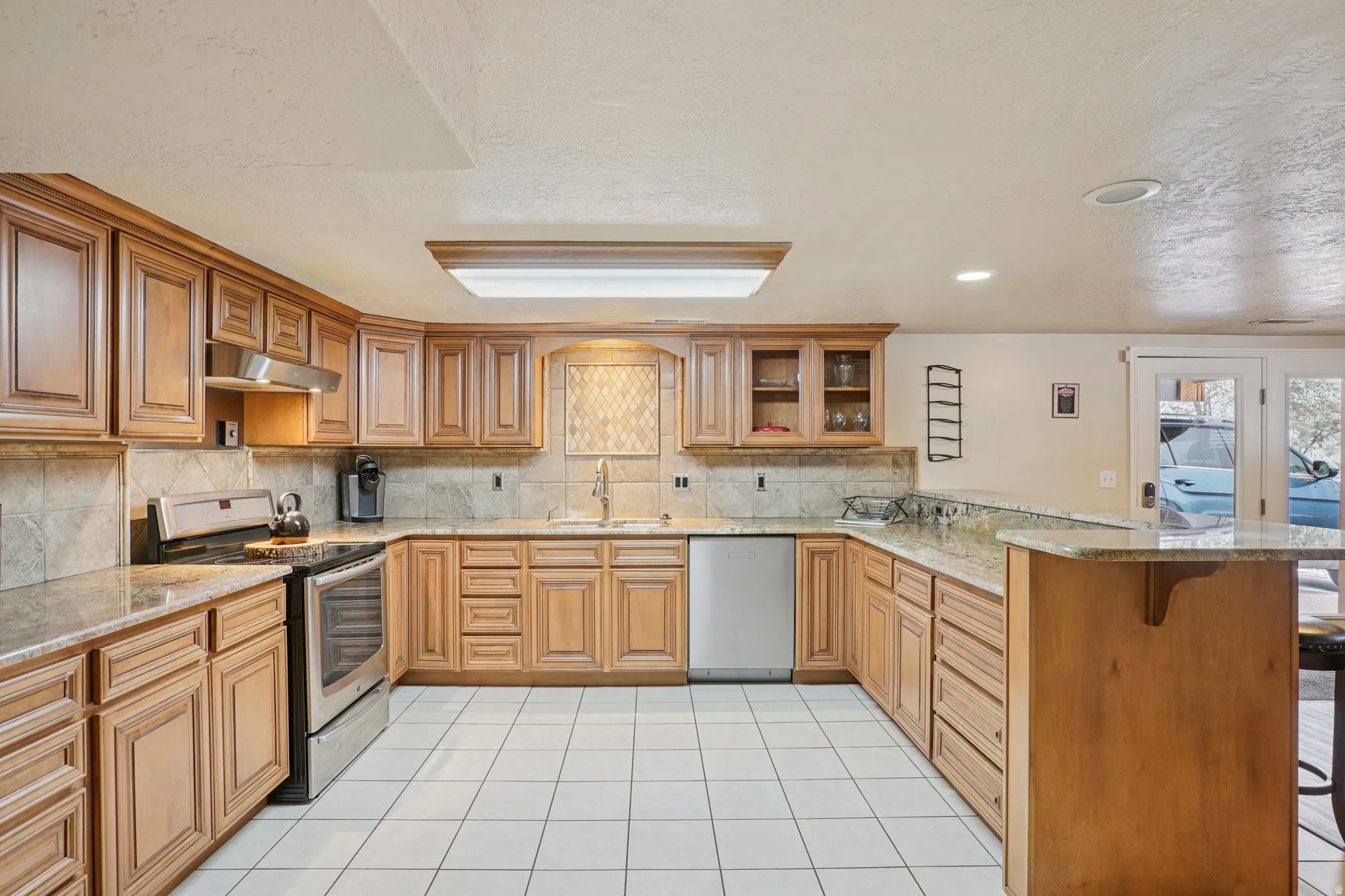 Kitchen with a peninsula, a breakfast bar, stainless steel appliances, glass fronted cabinets, and wood finish cabinets