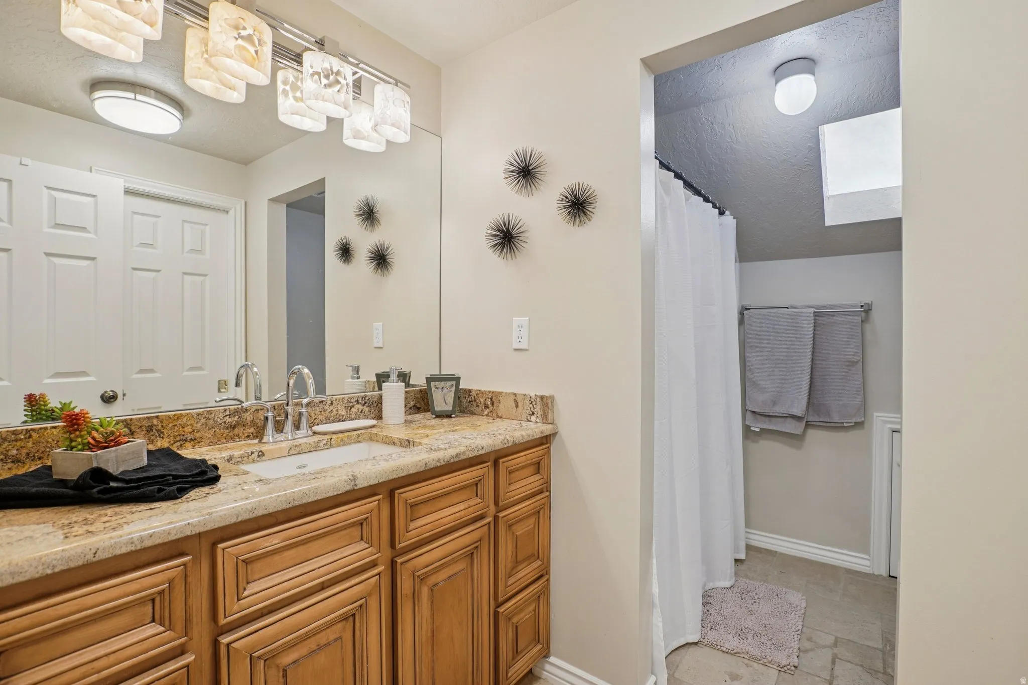 Bathroom with vanity, a shower with curtain, and light stone finish floors