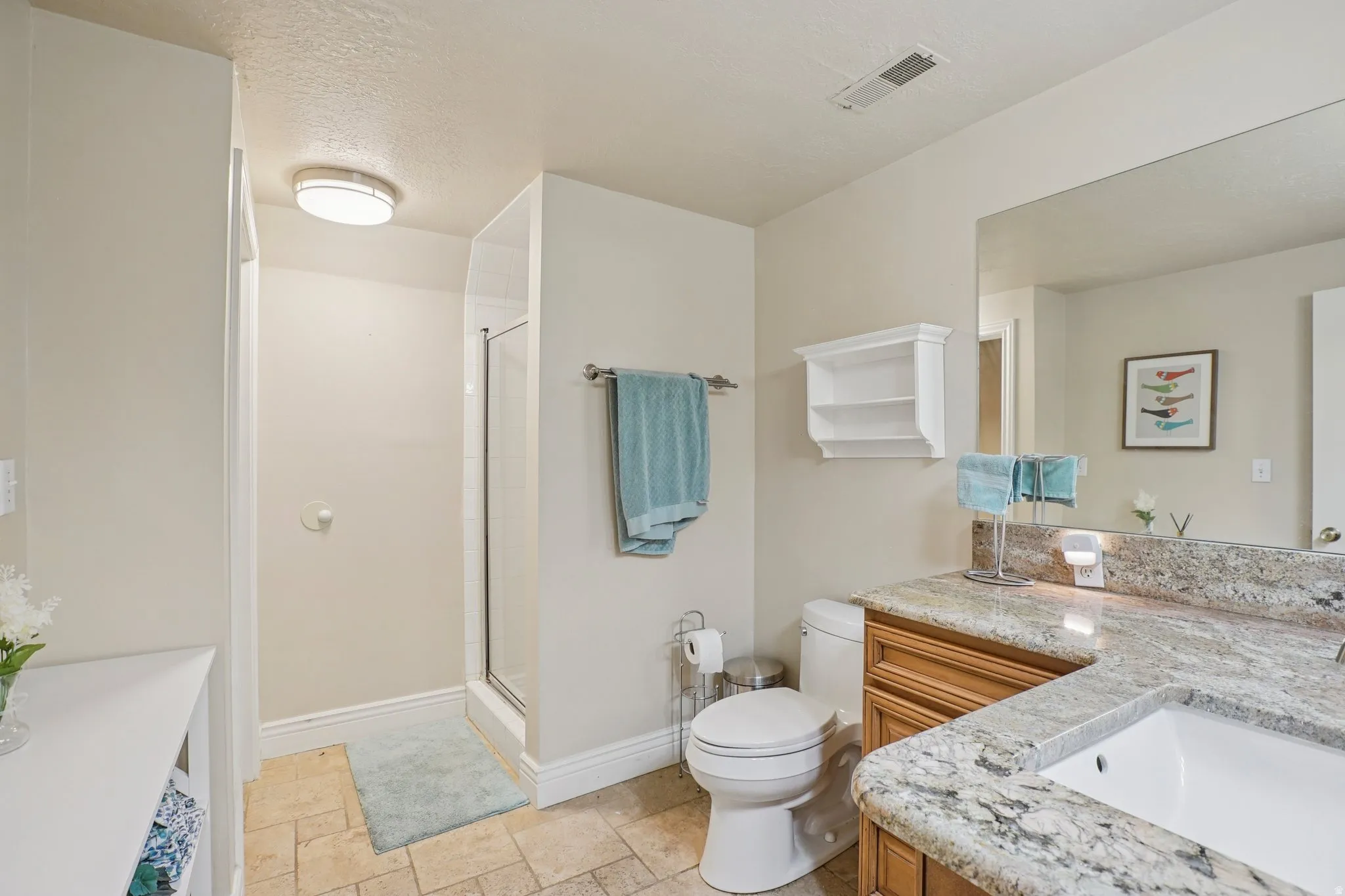 Full bath with vanity, a shower stall, light stone finish floors, and a textured ceiling