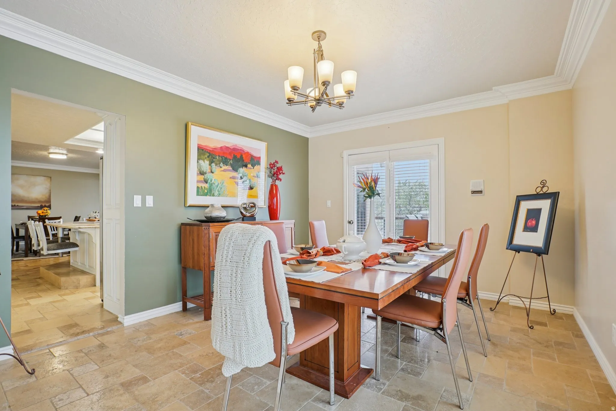 Dining area featuring stone tile flooring, crown molding, and a chandelier