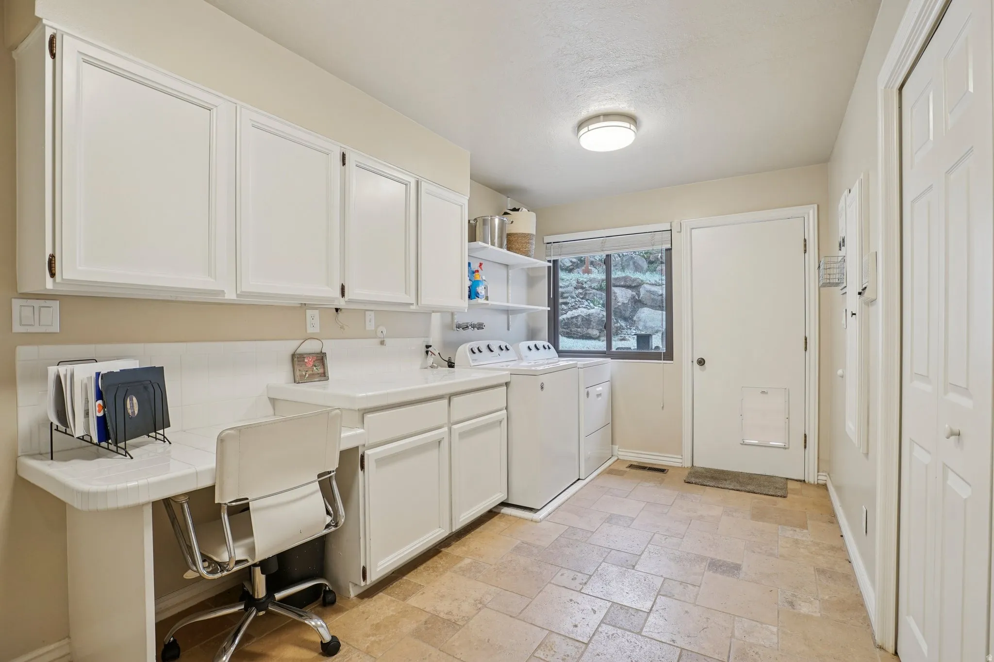 Laundry area featuring stone tile floors, washing machine and dryer, an office area, and cabinet space