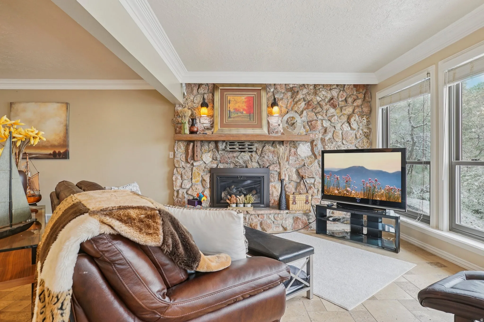 Living area featuring ornamental molding, a stone fireplace, stone tile flooring, and a textured ceiling