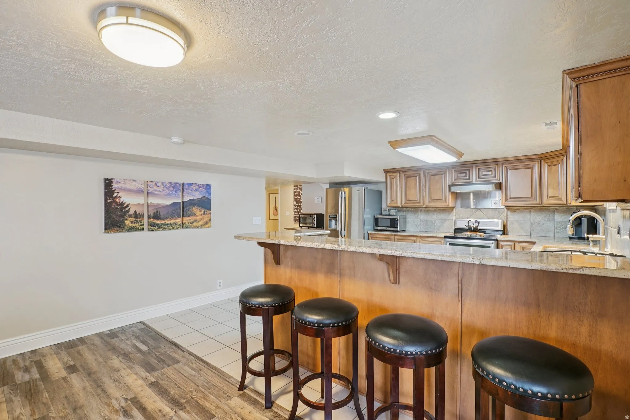Kitchen featuring light stone countertops, a peninsula, a breakfast bar, a textured ceiling, and light wood-type flooring