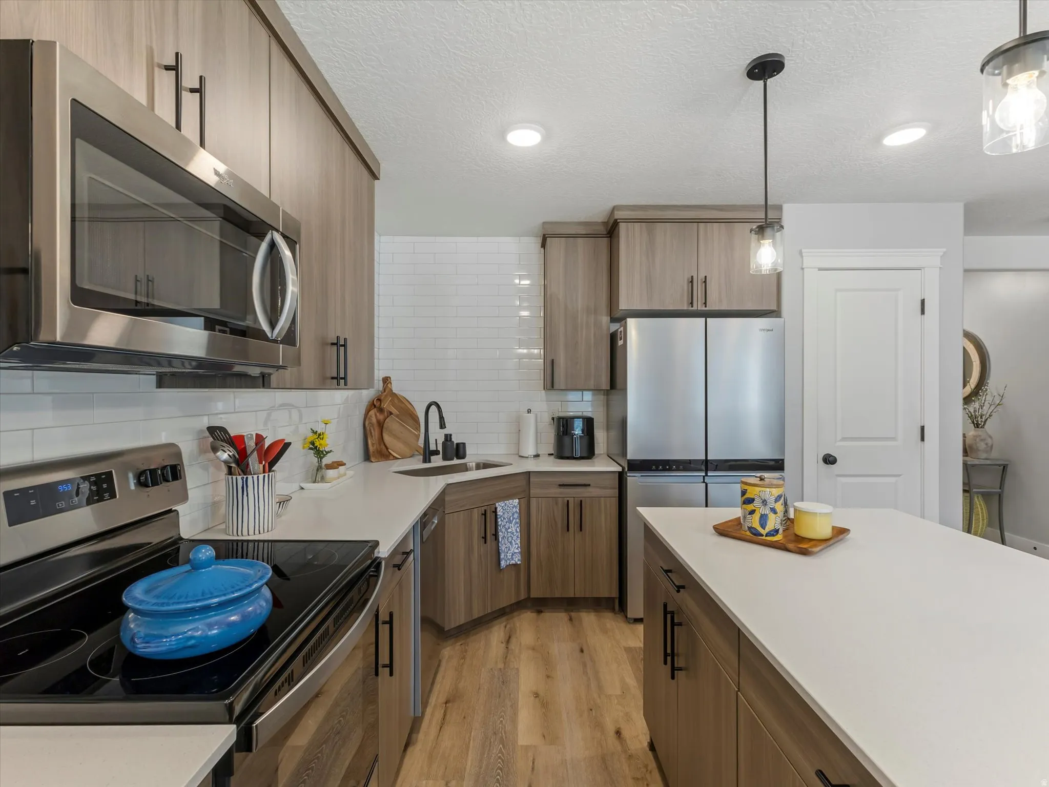 Kitchen featuring stainless steel appliances, light wood finished floors, decorative backsplash, decorative light fixtures, and wood finish cabinetry