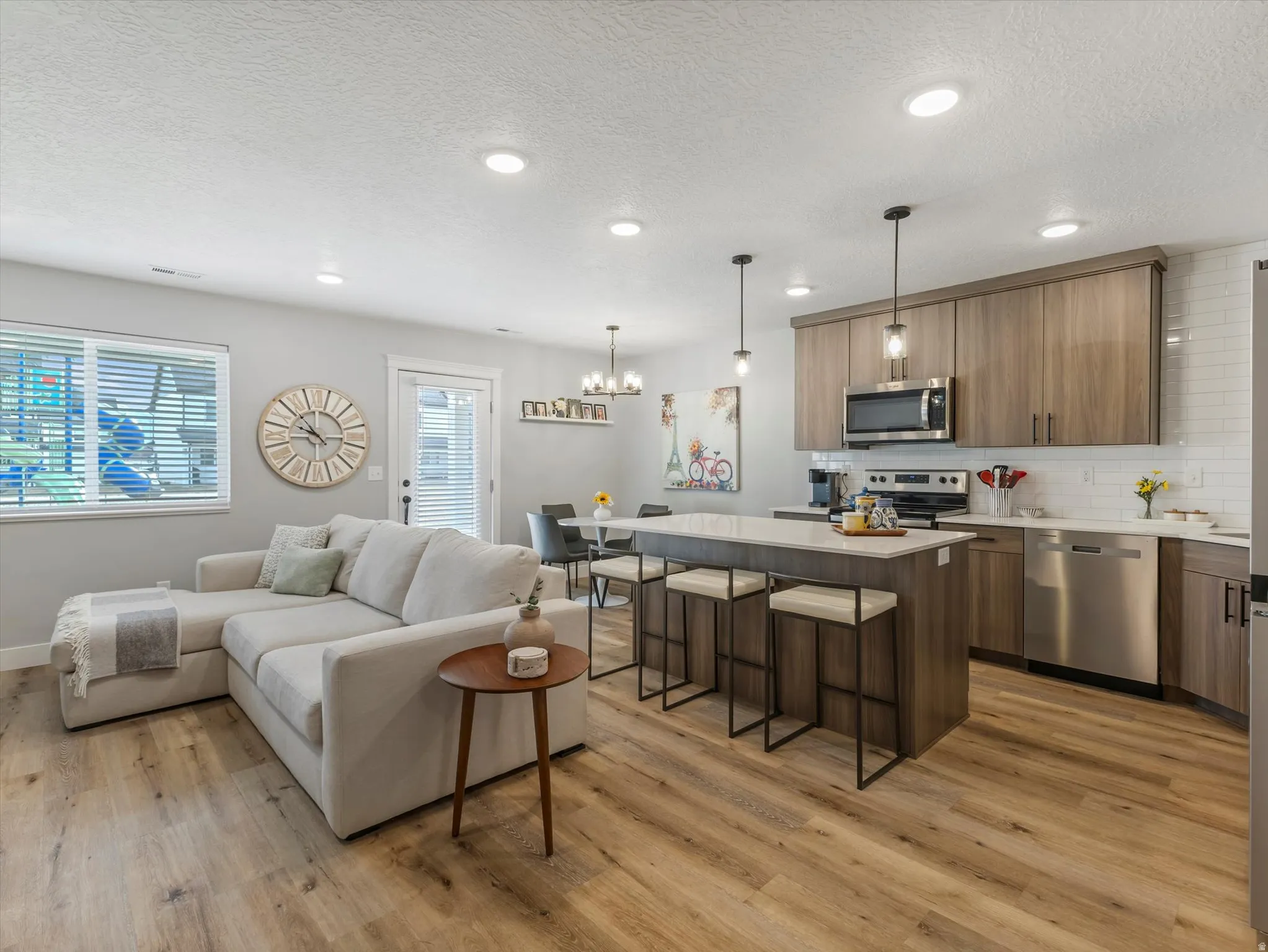 Living room with light wood finished floors, a textured ceiling, and hanging lights