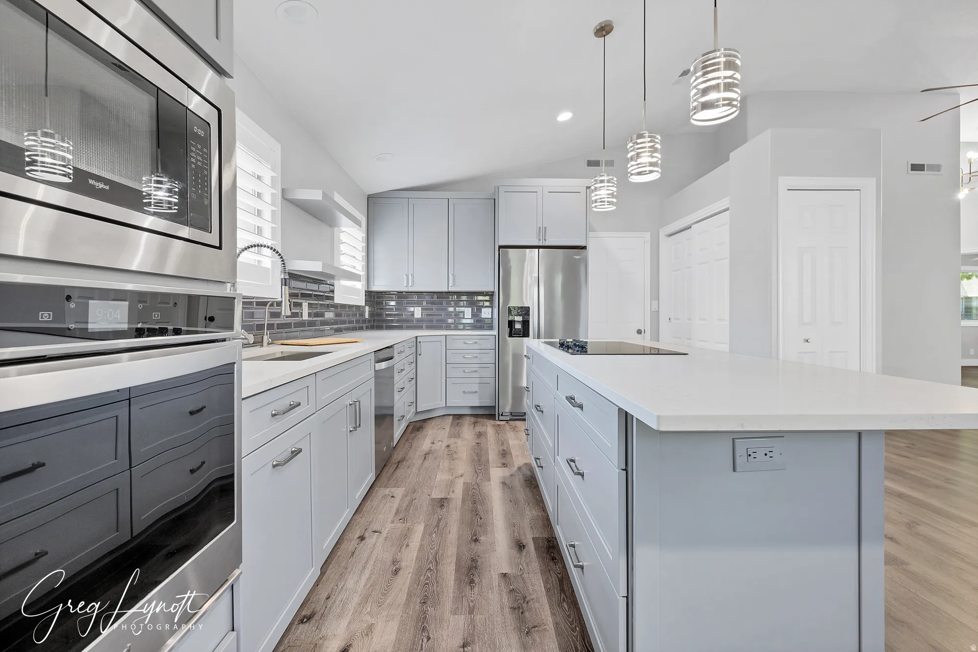 Kitchen with gray cabinetry, stainless steel appliances, light wood finished floors, a center island, and vaulted ceiling