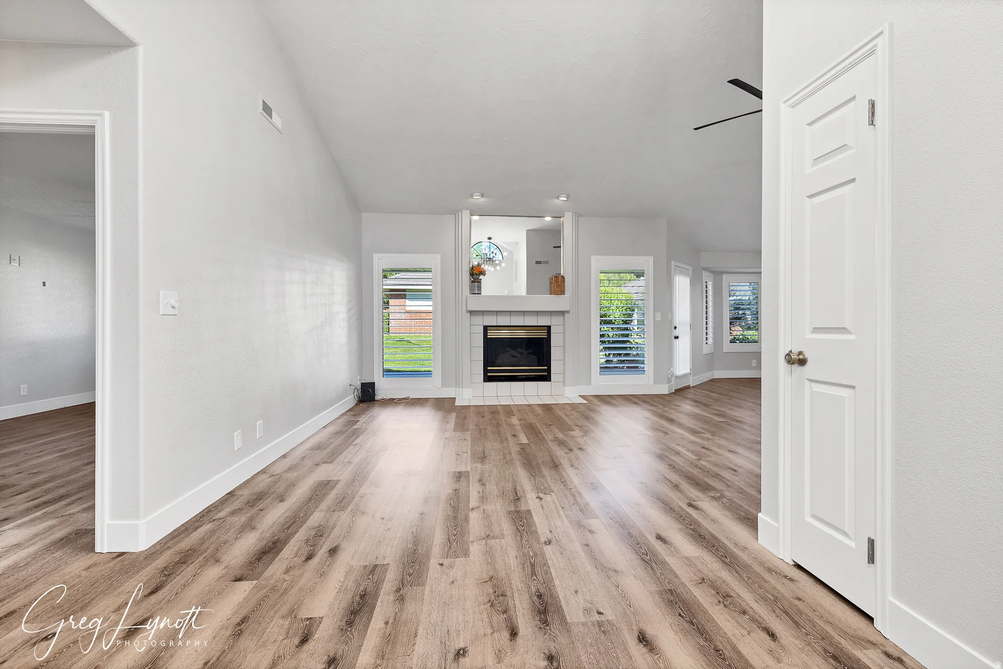 Unfurnished living room featuring lofted ceiling, light wood finished floors, healthy amount of natural light, a tiled fireplace, and a ceiling fan