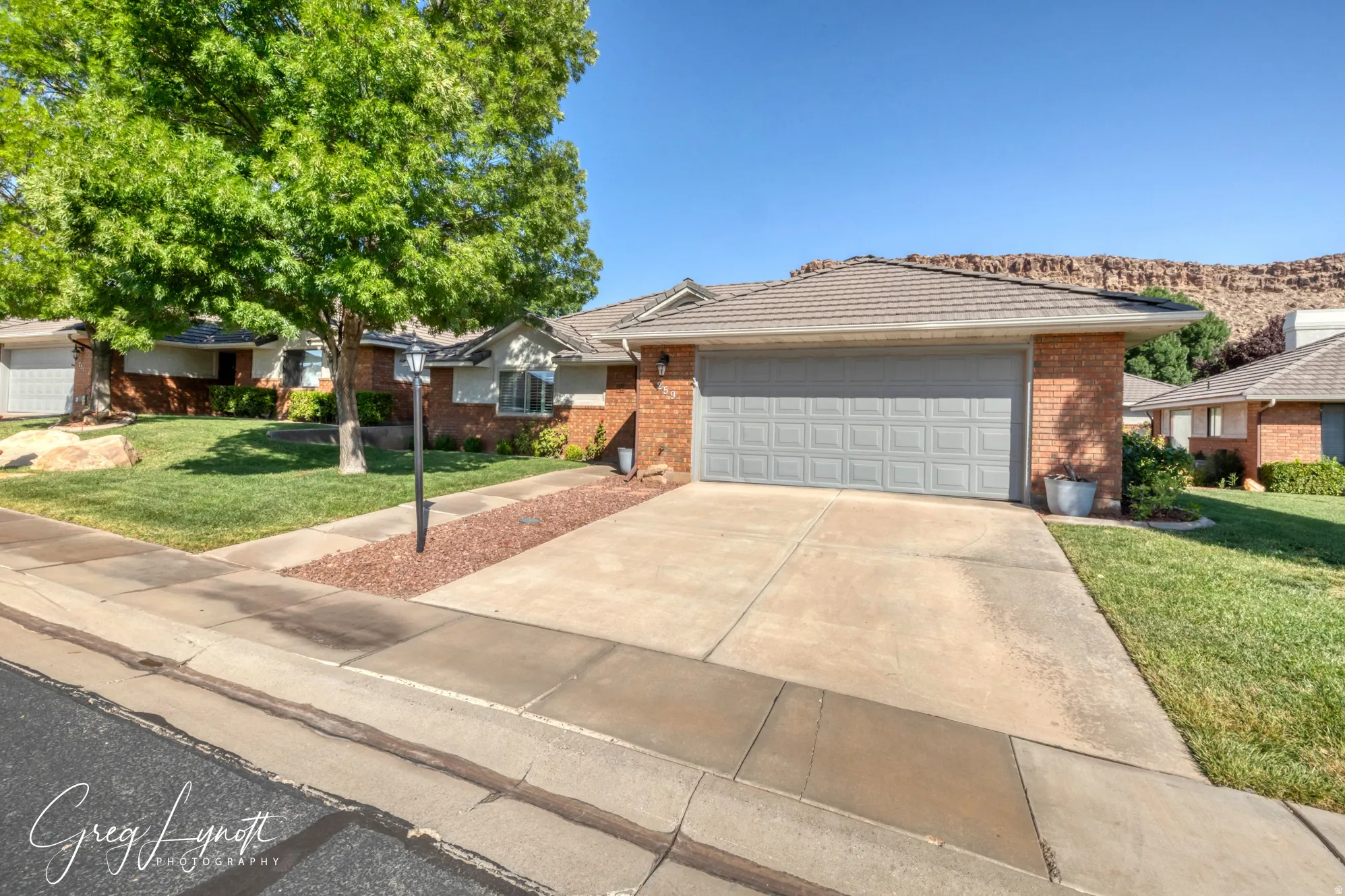 Ranch-style house with a front yard, driveway, brick siding, a tile roof, and a garage