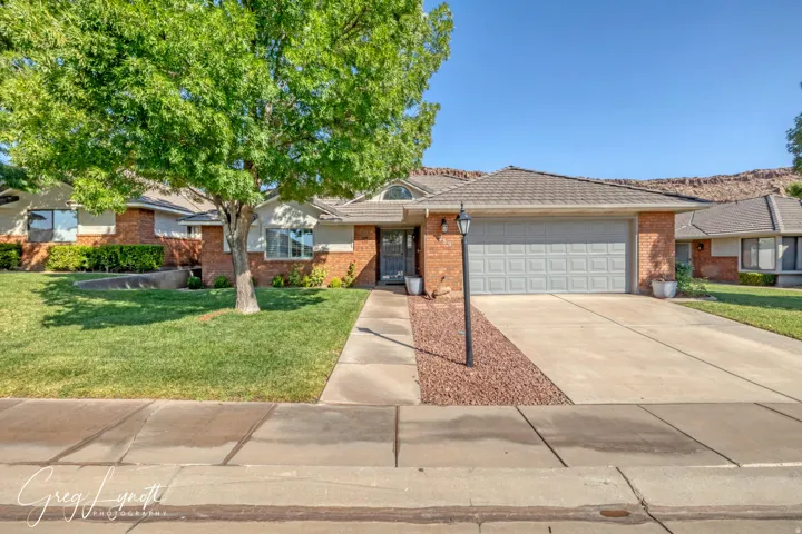 Ranch-style home with a front yard, concrete driveway, a garage, brick siding, and a tiled roof