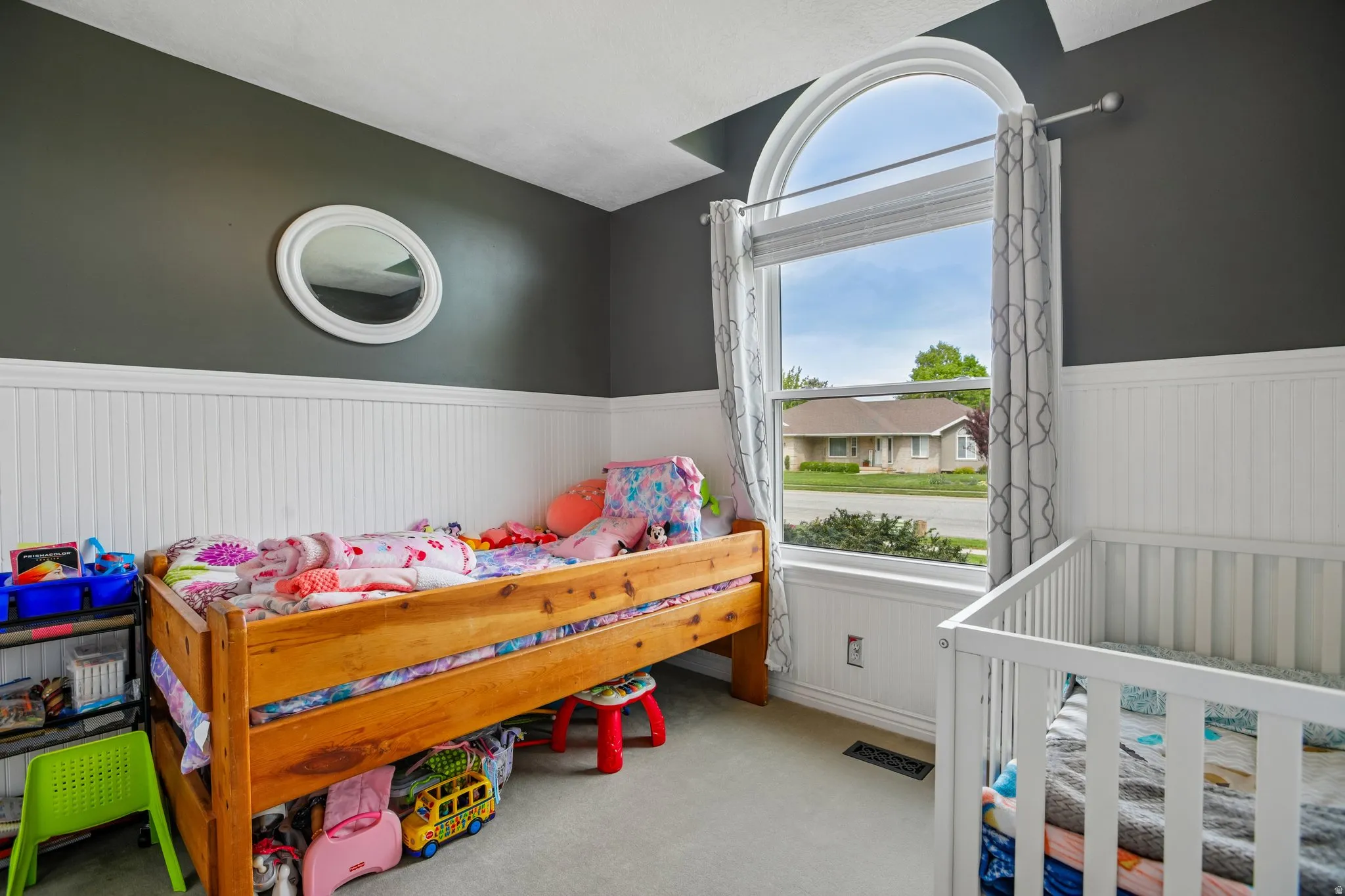 Bedroom featuring wainscoting, light carpet, and a crib