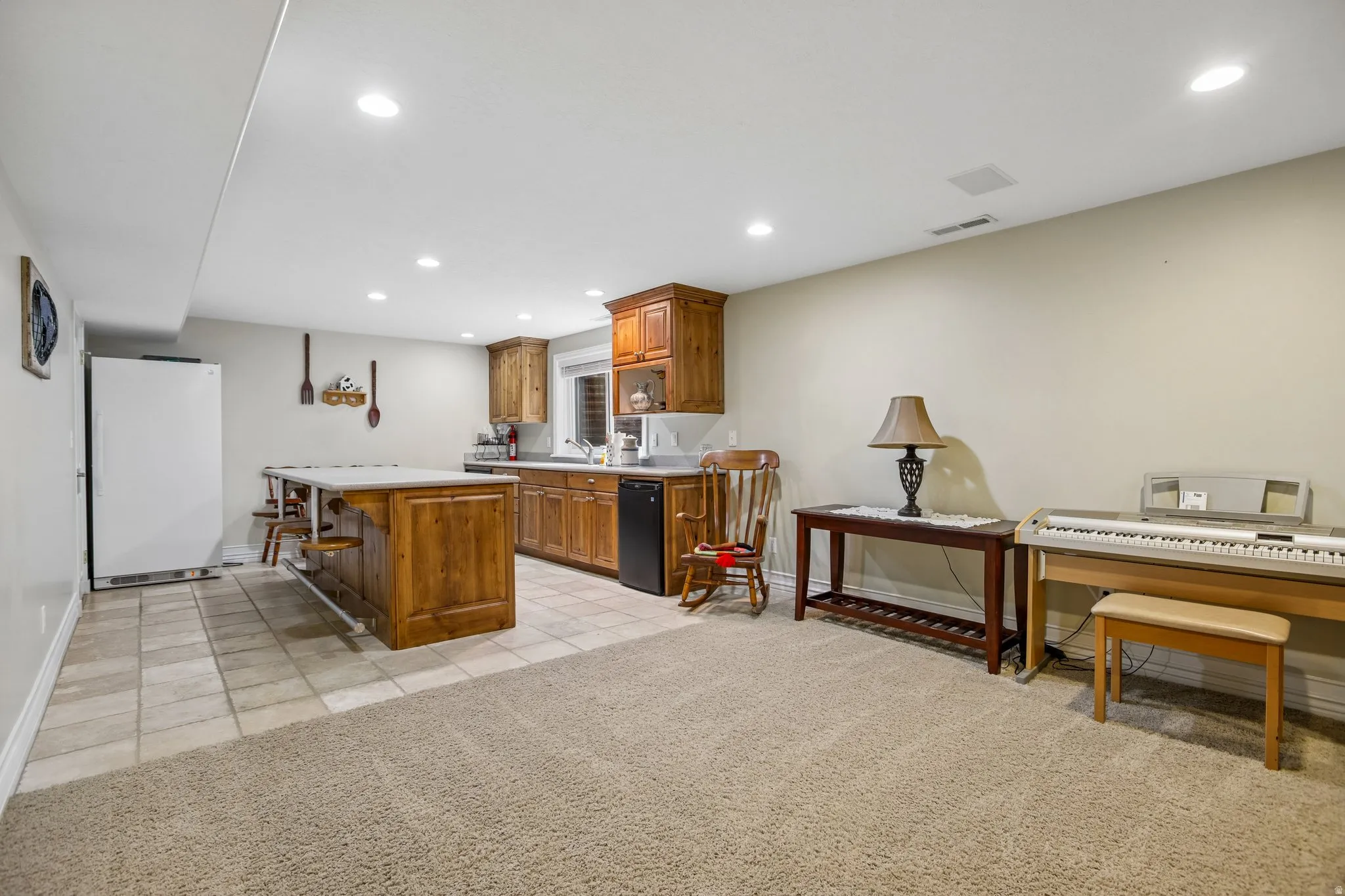Kitchen featuring wood finish cabinetry, light countertops, freestanding refrigerator, recessed lighting, and a center island