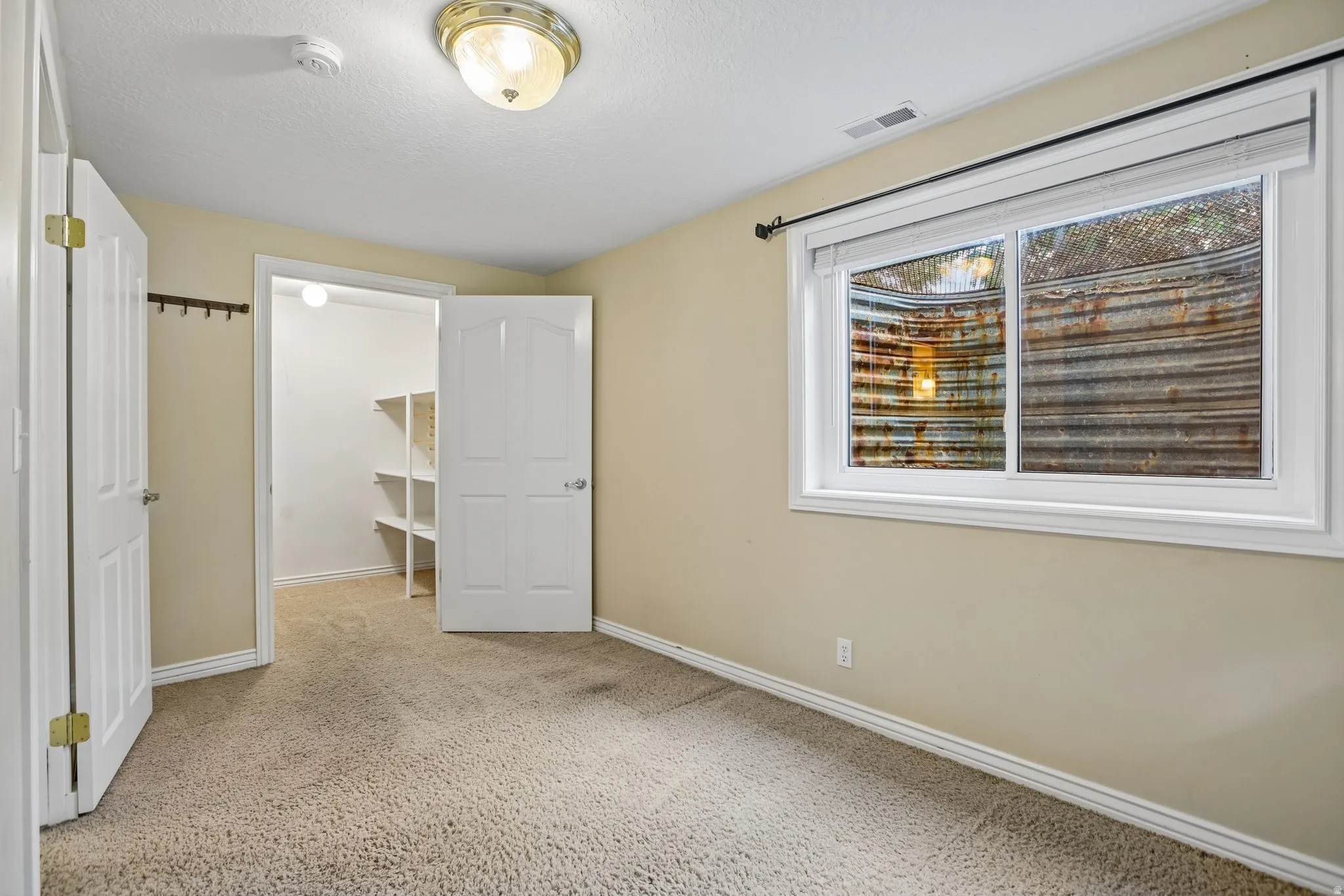 Unfurnished bedroom with a spacious closet, light carpet, and a textured ceiling