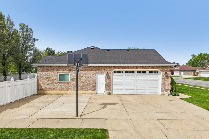 View of property exterior featuring a patio, brick siding, roof with shingles, driveway, and a garage