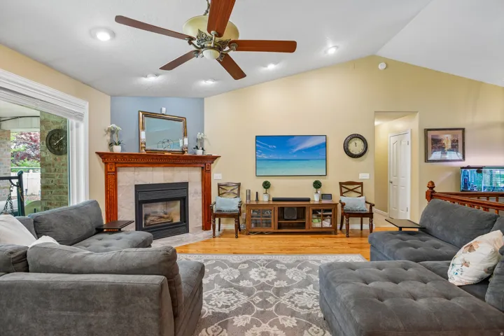 Living room with ceiling fan, a tile fireplace, wood finished floors, and recessed lighting