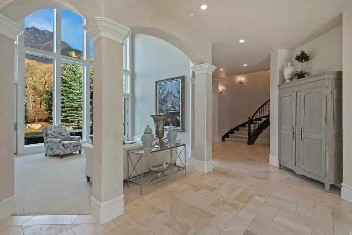 Hall featuring arched walkways, ornate columns, light colored carpet, stone tile flooring, and a high ceiling