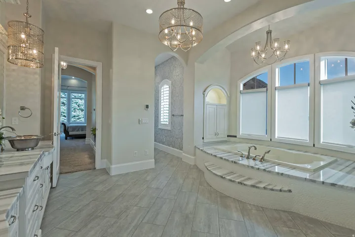 Ensuite bathroom with a chandelier, vanity, a garden tub, and healthy amount of natural light