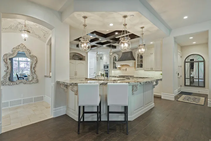 Kitchen with light stone countertops, white cabinetry, hanging light fixtures, decorative backsplash, and a breakfast bar area