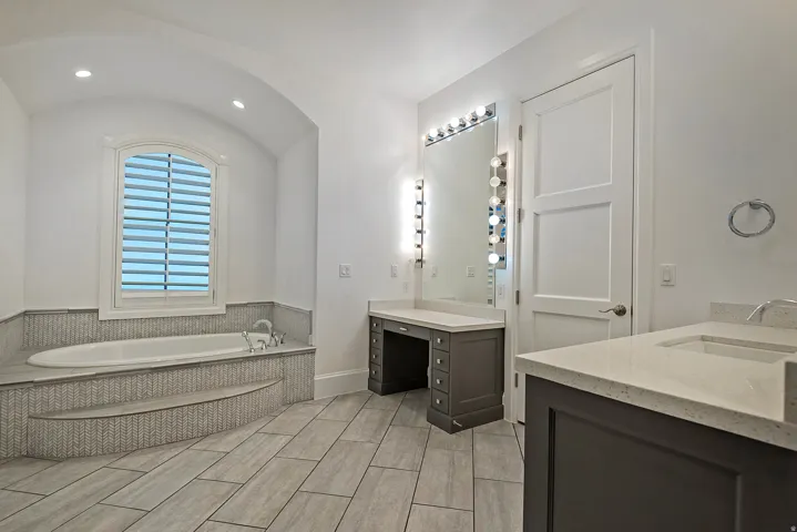 Bathroom with a bath, two vanities, recessed lighting, and lofted ceiling
