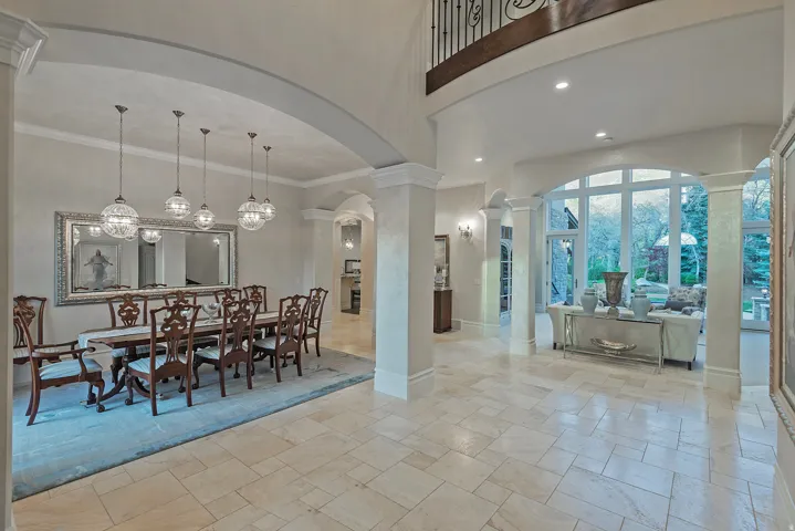 Dining area with ornate columns, stone tile floors, crown molding, hanging lights, and arched walkways