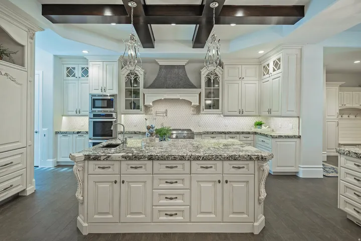 Kitchen featuring glass fronted cabinets, coffered ceiling, dark wood-style flooring, light stone counters, and a center island with sink