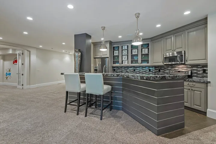 Kitchen with gray cabinets, a breakfast bar, a kitchen island with sink, stainless steel appliances, and tasteful backsplash