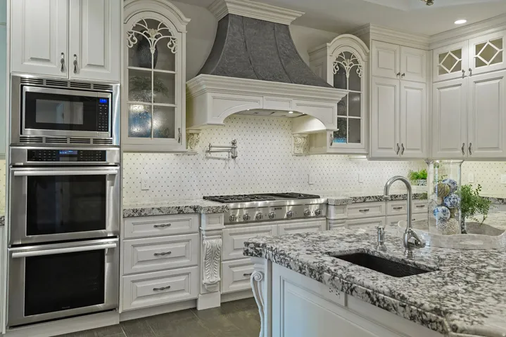 Kitchen featuring glass insert cabinets, stainless steel appliances, white cabinetry, light stone countertops, and backsplash
