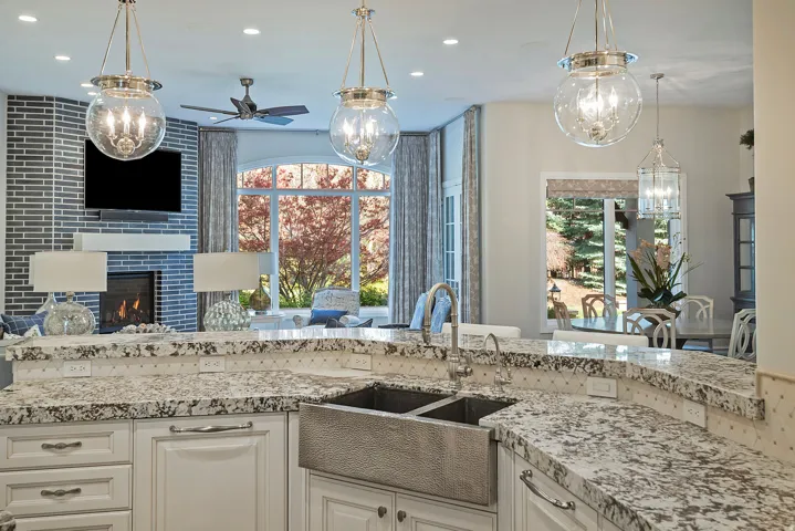 Kitchen with ceiling fan, light stone countertops, white cabinetry, a tiled fireplace, and open floor plan