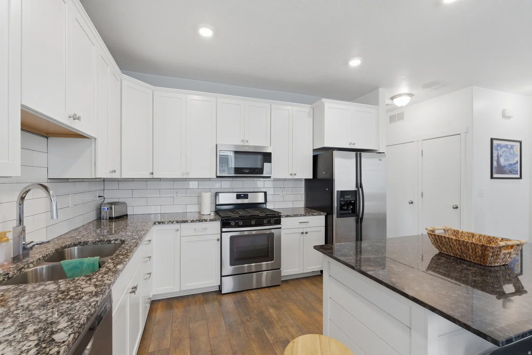 Kitchen with dark stone counters, stainless steel appliances, white cabinets, dark wood-style floors, and decorative backsplash