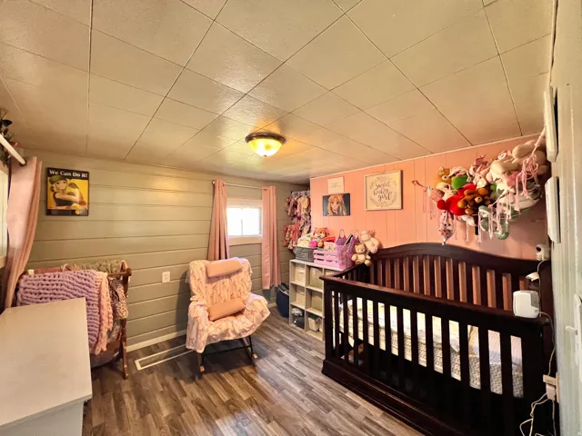 Bedroom with a nursery area, dark wood-style flooring, and wooden walls