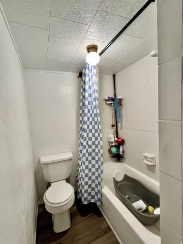 Full bath with dark wood-style flooring and shower / bath combination with curtain