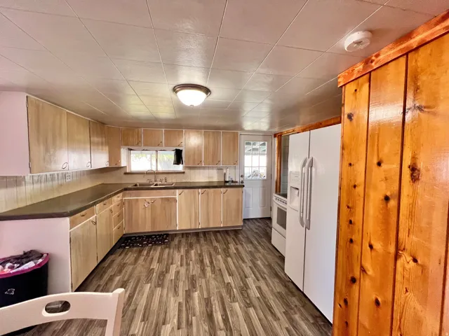 Kitchen featuring dark countertops, white appliances, dark wood finished floors, and light wood finish cabinets