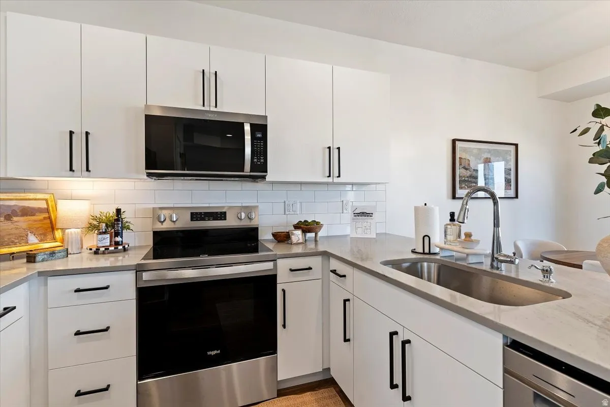 Kitchen featuring stainless steel appliances, white cabinets, light stone counters, and tasteful backsplash