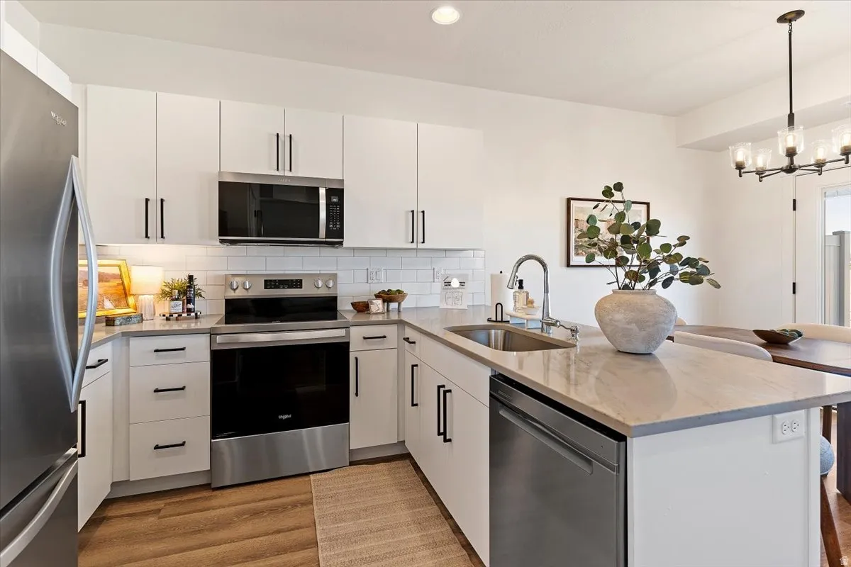 Kitchen featuring stainless steel appliances, light stone countertops, a peninsula, and white cabinetry