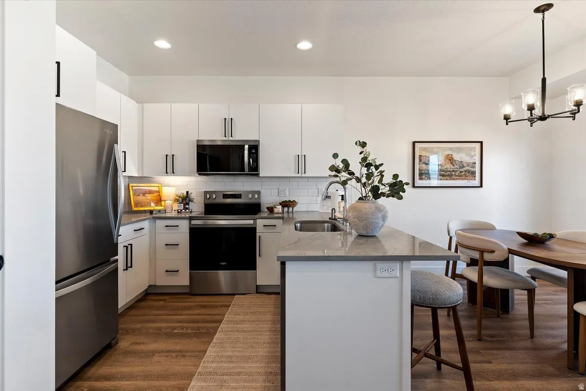 Kitchen featuring a peninsula, stainless steel appliances, white cabinetry, dark wood-style flooring, and a kitchen bar